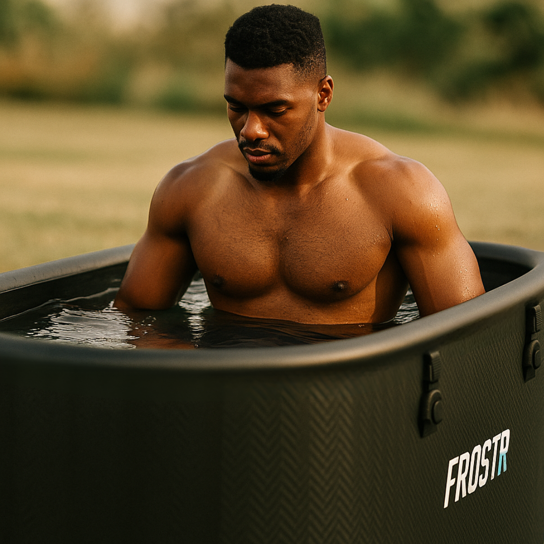 Man sitting in a black ice bath / cold plunge tub labeled 'FROSTR' with a blurred natural background